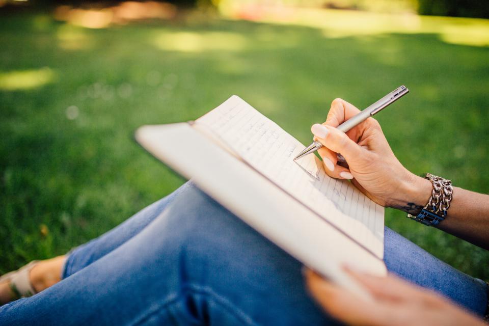 Persona joven escribiendo su currículum en un cuaderno al aire libre